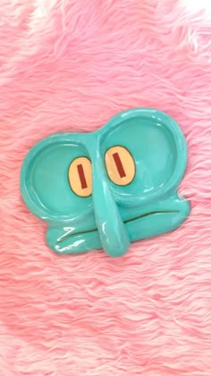 a blue frog shaped object with two eyes on pink fur covered surface, looking at the camera