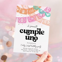 a person holding up a card with the words cumple uno on it in front of some confetti