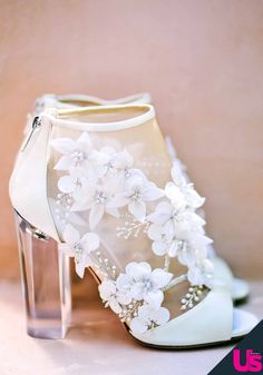 a pair of white high heel shoes with flowers on the side and clear heels in front