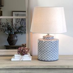 a lamp sitting on top of a wooden table next to a mirror and vase with flowers