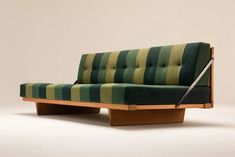 a green and yellow striped couch sitting on top of a wooden table next to a white wall