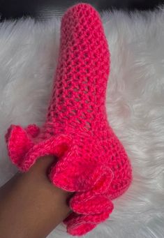 a hand holding a pink crocheted boot on top of a white fur rug