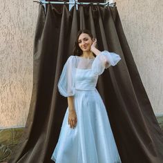 a woman standing in front of a curtain wearing a white dress with puffy sleeves