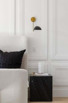 a black and white pillow sitting on top of a white chair next to a lamp