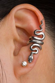 a woman's ear is adorned with two silver snakes and a white diamond in the middle