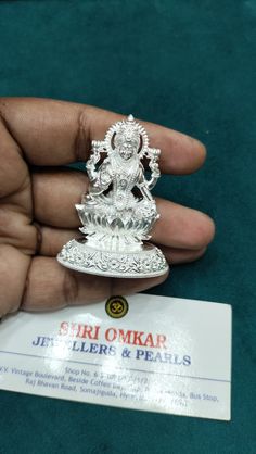 a person holding a small silver statue on top of a green cloth covered table next to a business card