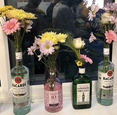 three bottles with flowers in them sitting on a window sill next to each other