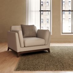 a chair sitting in front of two windows on top of a wooden floor next to a rug