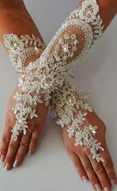 a woman's hands with white lace and flowers on them, both wearing gloves