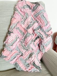 a pink and gray blanket sitting on top of a couch next to a teddy bear