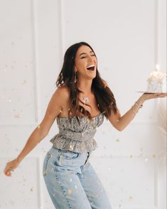 a woman holding a cake and laughing with confetti falling from her hands in the air