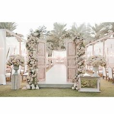 an outdoor ceremony setup with white flowers and greenery on the aisle, surrounded by wooden doors