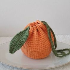 an orange crocheted bag sitting on top of a white plate with a green leaf