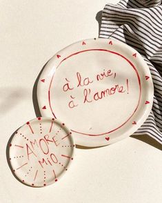 two white plates with red writing on them next to a blue and white striped napkin