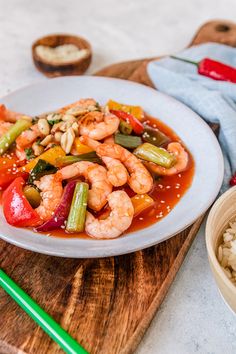 a white plate topped with shrimp and veggies on top of rice next to chopsticks