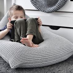 a little boy sitting on a bean bag chair with his feet propped up in the air