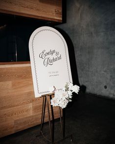 a sign with flowers on it sitting in front of a wooden wall next to a door