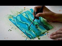 a person is painting on a piece of paper with watercolors and paintbrushes