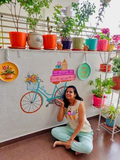 a woman sitting on the floor in front of a wall with potted plants