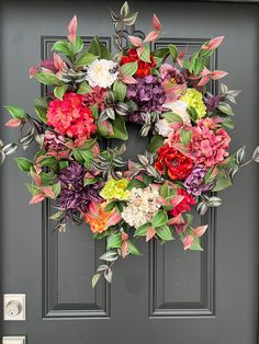 a colorful wreath on the front door of a house with green leaves and pink flowers