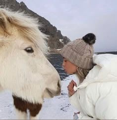 a woman standing next to a white horse in the snow