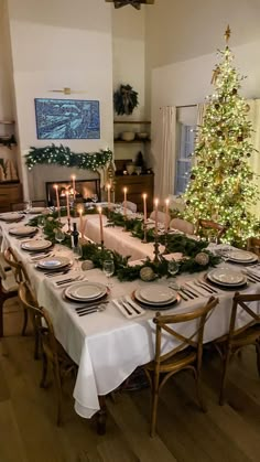 a dining room table is set for christmas dinner with candles and greenery on it