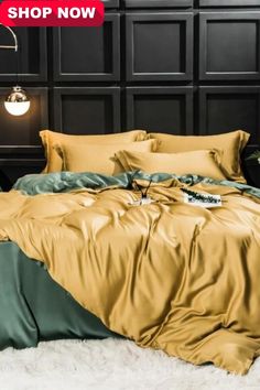 an image of a bed with gold sheets and pillows on the floor in front of a black wall