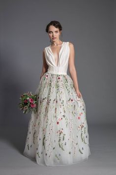 a woman in a white dress with flowers on the skirt is standing against a gray background