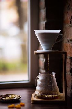 coffee being poured into a cup on top of a wooden table next to a window