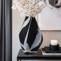 a black and white vase with flowers in it on a table next to a candle