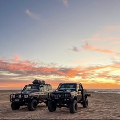 two off road vehicles parked on the beach at sunset or sunrise with an ocean in the background