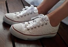 a pair of white shoes with pearls on them sitting on a wooden floor next to a person's legs