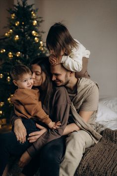 a man and two children sitting on top of a couch next to a christmas tree