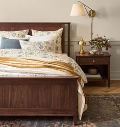 a bed sitting on top of a wooden floor next to a night stand and lamp