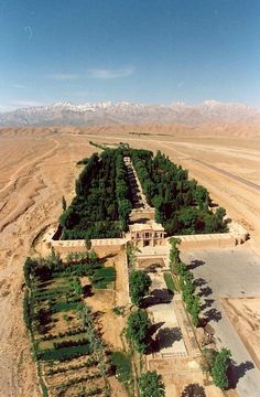 an aerial view of a large building in the middle of some dirt land with mountains in the background