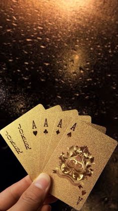 four gold playing cards held up in front of a dark background with light shining on them