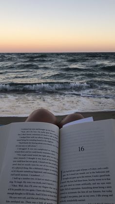 an open book sitting on top of a beach next to the ocean