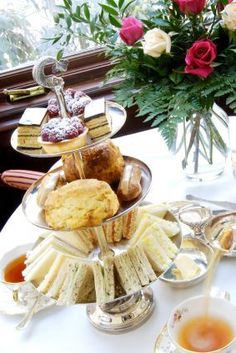 an assortment of pastries and tea on a table in front of a vase with roses