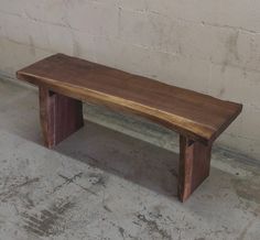 a wooden bench sitting in front of a white brick wall and cement floored area