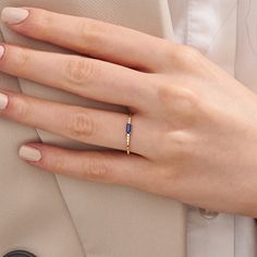 a woman's hand wearing a gold ring with a blue bead on it