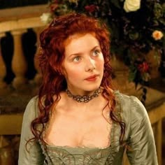 a woman with red hair and blue eyes in a green dress is looking at the camera