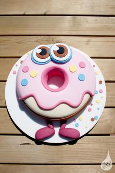 a pink cake with googly eyes sitting on top of a wooden table next to a white plate