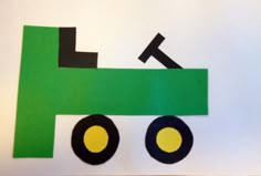 paper cut out of the shape of a green truck with black wheels and yellow eyes