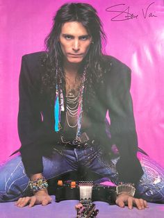 a man with long hair sitting on top of a table next to a pink background