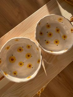 two white bowls with yellow flowers on them sitting on a wooden table next to each other