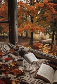 an open book and cup sit on a window sill in front of autumn leaves