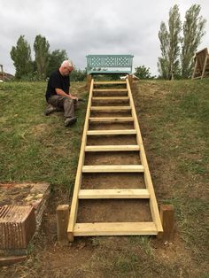 a man sitting on top of a set of stairs next to a green bench in the grass