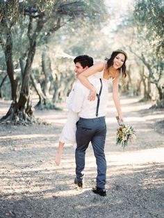 a man carrying a woman on his back while walking through an olive tree filled forest