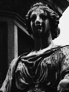 black and white photograph of a statue with her hands on her hips, in front of a building