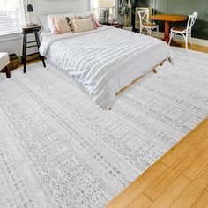 a large white bed sitting in a bedroom on top of a hard wood floor next to a window